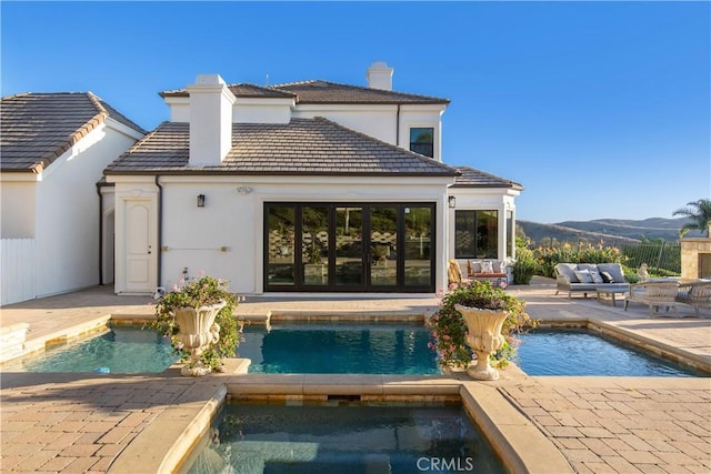 rear view of property with a patio area, a swimming pool with hot tub, a mountain view, and an outbuilding