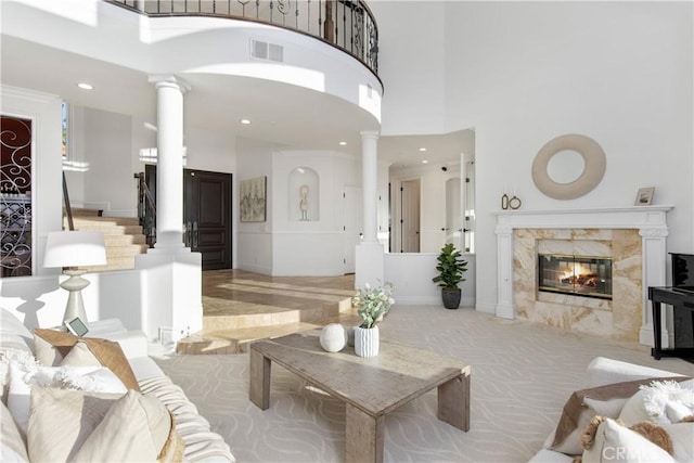 carpeted living room with a premium fireplace, a high ceiling, and ornate columns