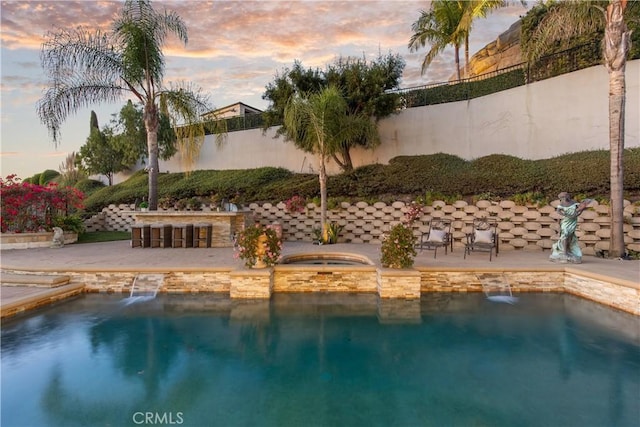 pool at dusk with pool water feature, a patio area, and exterior bar