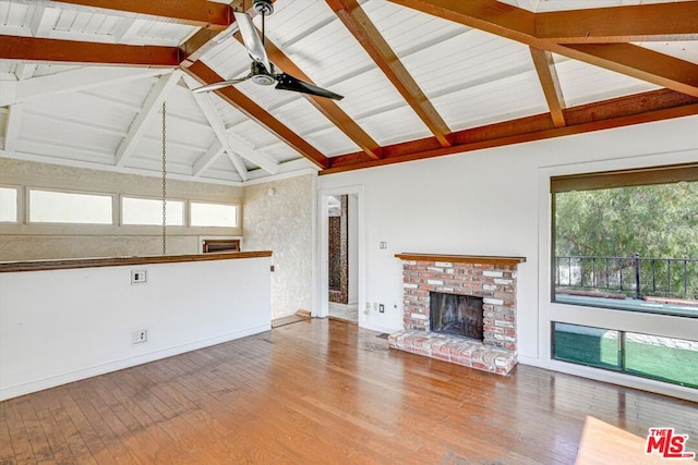 unfurnished living room featuring beam ceiling, a healthy amount of sunlight, a brick fireplace, and hardwood / wood-style floors