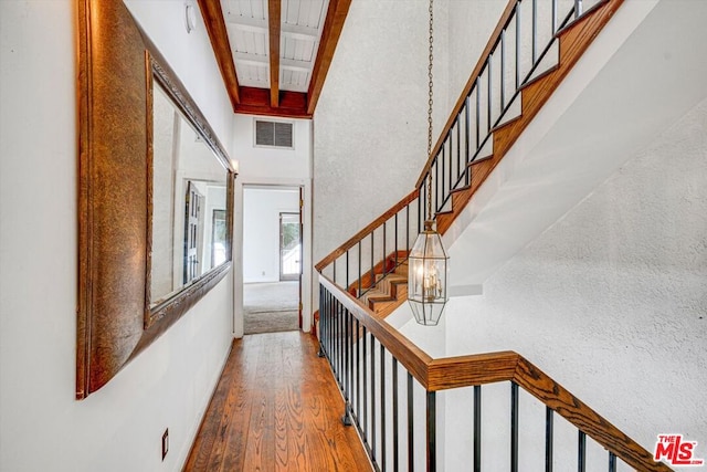 corridor featuring beam ceiling, a high ceiling, a chandelier, and hardwood / wood-style flooring