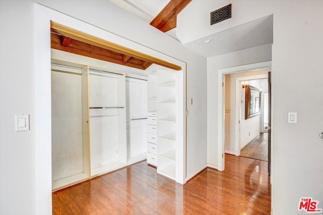 unfurnished bedroom with a closet, wood-type flooring, and beamed ceiling