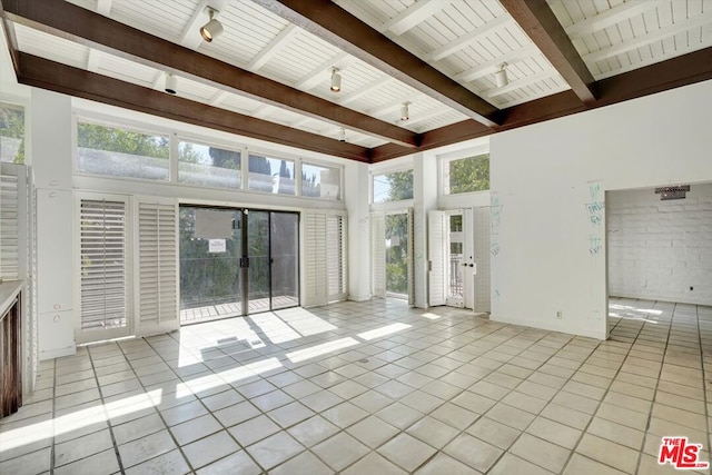 unfurnished living room featuring a wealth of natural light, light tile patterned floors, beam ceiling, and a towering ceiling