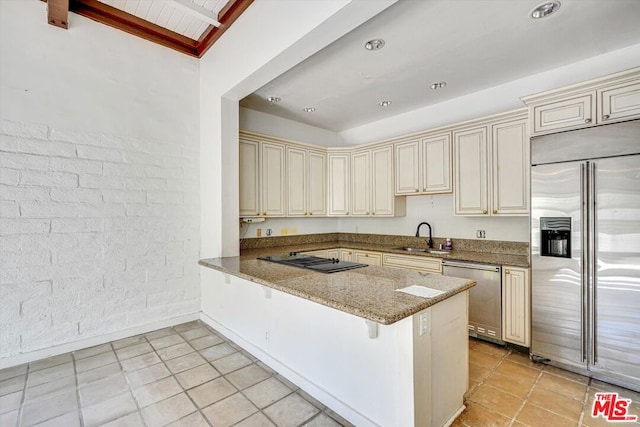 kitchen featuring kitchen peninsula, a kitchen bar, light stone countertops, appliances with stainless steel finishes, and cream cabinets