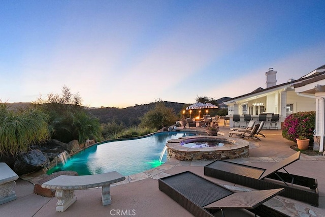 pool at dusk featuring an in ground hot tub, a patio area, and pool water feature