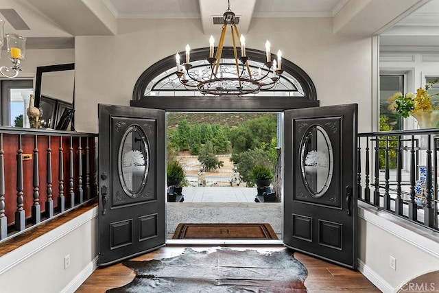 foyer featuring wood-type flooring, ornamental molding, a chandelier, and a healthy amount of sunlight