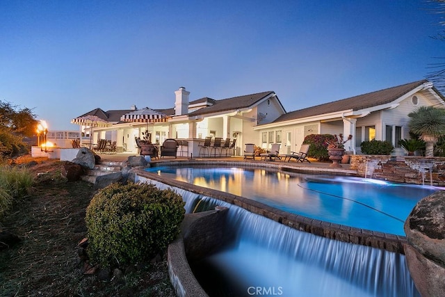 pool at dusk featuring pool water feature and a patio