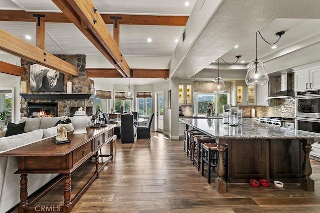 kitchen with pendant lighting, white cabinetry, dark wood-type flooring, a stone fireplace, and wall chimney exhaust hood