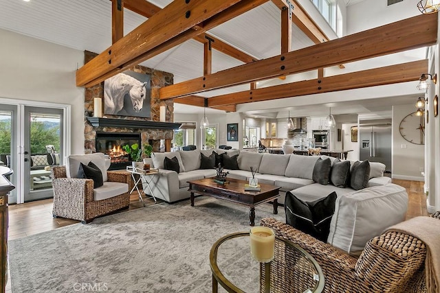 living room featuring a wealth of natural light, beamed ceiling, a stone fireplace, and high vaulted ceiling