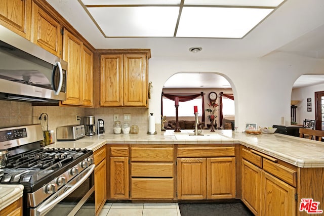 kitchen with light tile patterned floors, stainless steel appliances, backsplash, and kitchen peninsula