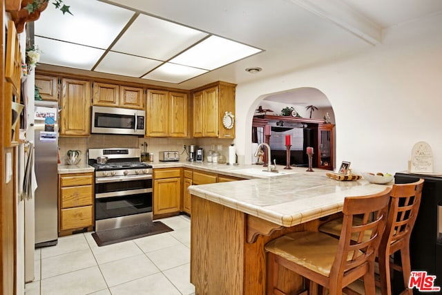 kitchen with kitchen peninsula, appliances with stainless steel finishes, tile counters, light tile patterned flooring, and sink