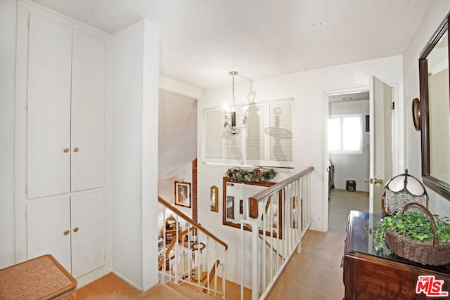 hallway with light colored carpet, an inviting chandelier, and a textured ceiling