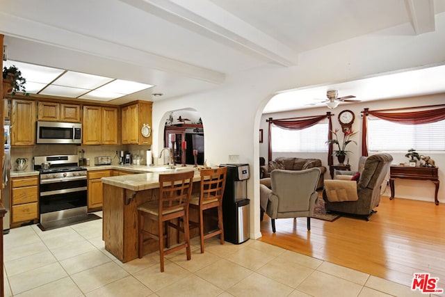 kitchen featuring ceiling fan, kitchen peninsula, appliances with stainless steel finishes, a kitchen breakfast bar, and light tile patterned floors