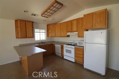 kitchen featuring lofted ceiling, kitchen peninsula, sink, and white appliances