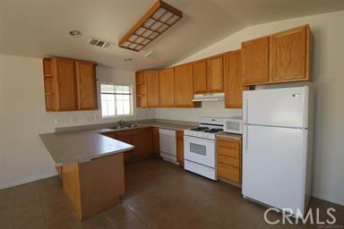 kitchen featuring sink, lofted ceiling, kitchen peninsula, and white appliances