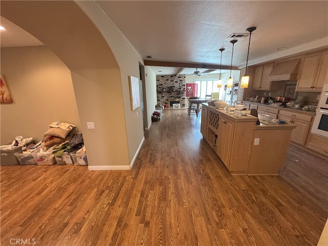 kitchen with decorative light fixtures, light brown cabinetry, dark hardwood / wood-style floors, and wall chimney range hood