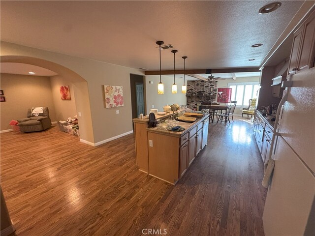 kitchen with ceiling fan, a fireplace, a center island, hanging light fixtures, and dark hardwood / wood-style flooring