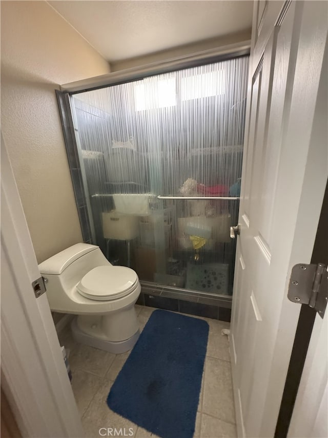 bathroom with toilet, tile patterned floors, and a shower with shower door