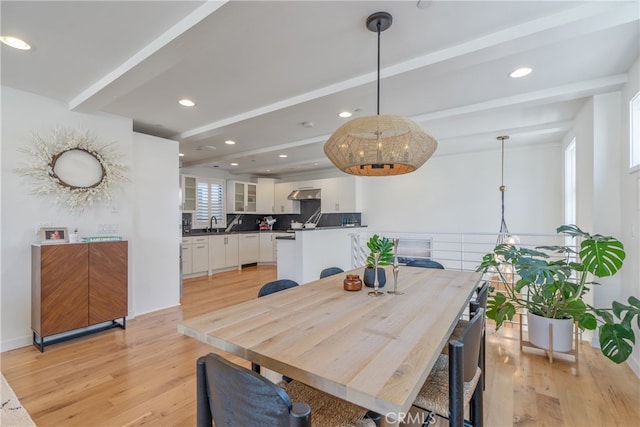 dining room featuring sink, light wood-type flooring, and beamed ceiling