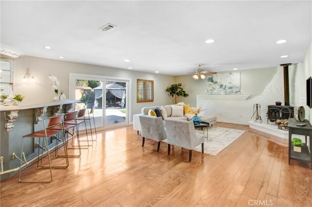 living room with ceiling fan, a wood stove, and light hardwood / wood-style flooring