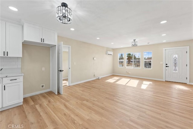 unfurnished living room with light hardwood / wood-style floors, an AC wall unit, and a notable chandelier