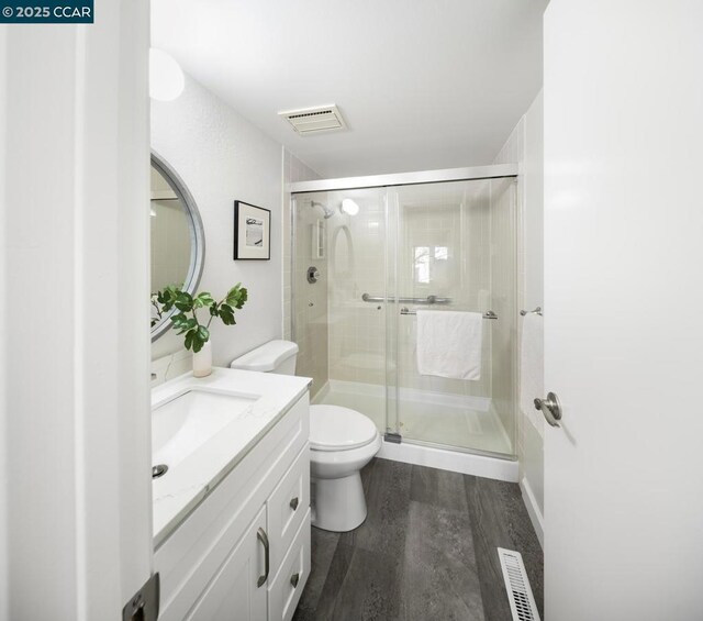 bathroom with hardwood / wood-style floors, toilet, a shower with door, and vanity