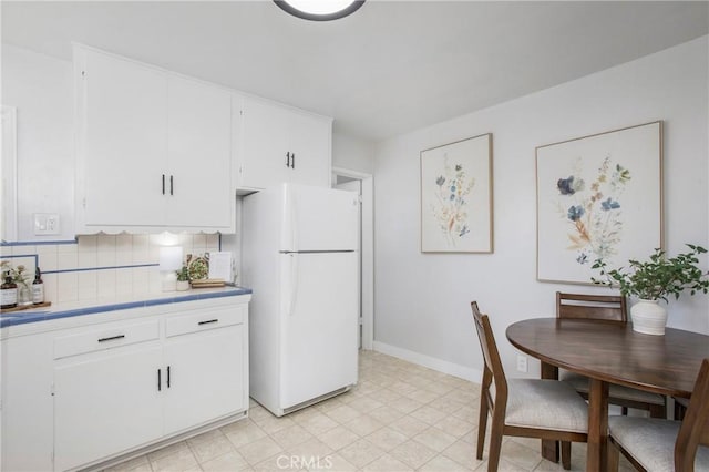 kitchen with white fridge, white cabinets, and tasteful backsplash