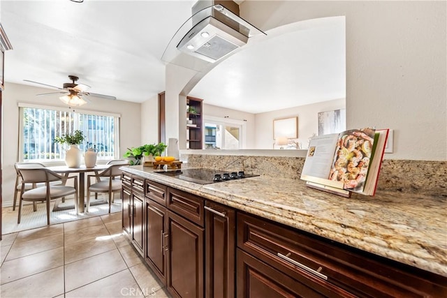 kitchen with light stone countertops, dark brown cabinetry, black electric stovetop, ceiling fan, and light tile patterned floors