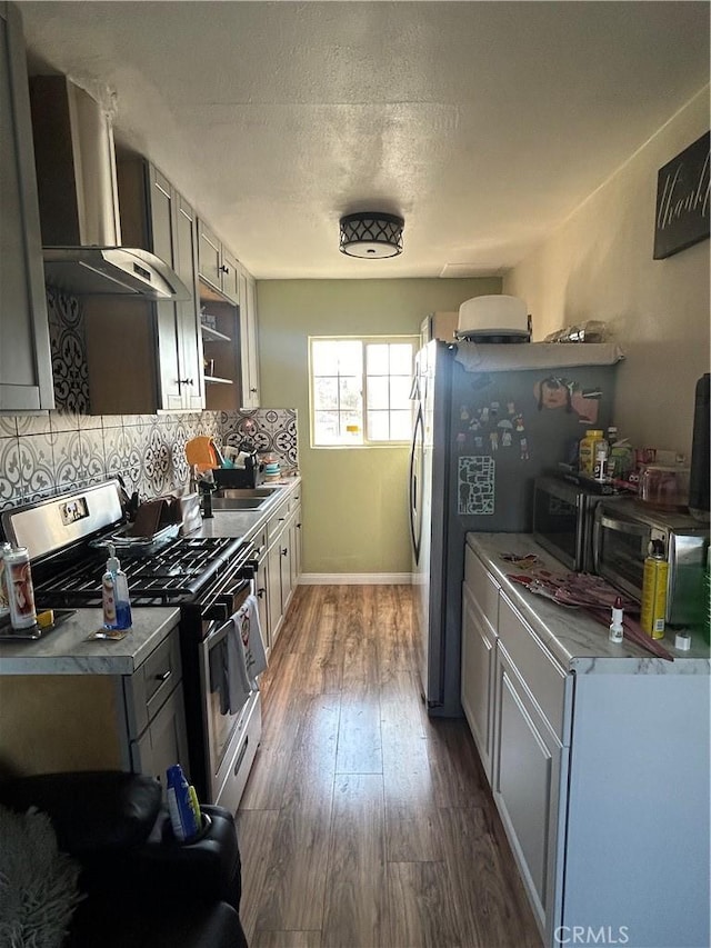 kitchen featuring gray cabinets, appliances with stainless steel finishes, dark hardwood / wood-style floors, tasteful backsplash, and wall chimney exhaust hood