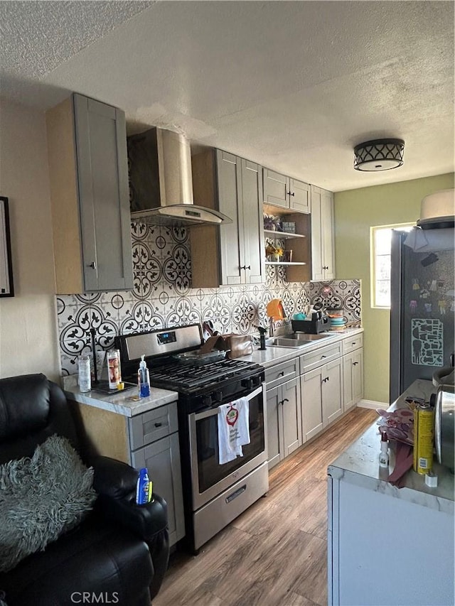 kitchen featuring appliances with stainless steel finishes, wall chimney exhaust hood, light hardwood / wood-style floors, backsplash, and gray cabinetry