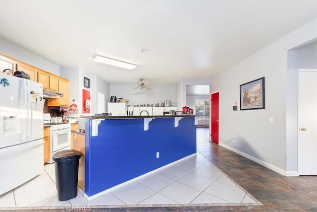 kitchen with ceiling fan, white appliances, light brown cabinets, a breakfast bar area, and light tile patterned floors