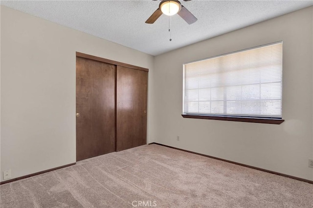 unfurnished bedroom with ceiling fan, light colored carpet, a textured ceiling, and a closet