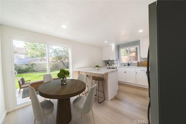 kitchen featuring a center island, a kitchen bar, black refrigerator, white cabinetry, and light hardwood / wood-style flooring