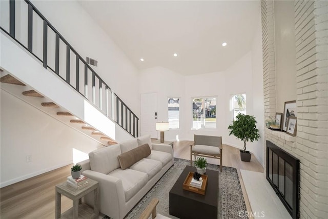 living room featuring a brick fireplace, a towering ceiling, and light hardwood / wood-style floors