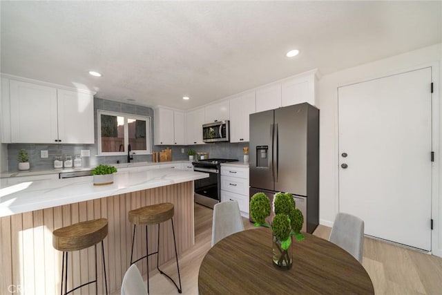 kitchen featuring light hardwood / wood-style floors, white cabinetry, light stone countertops, a kitchen breakfast bar, and stainless steel appliances