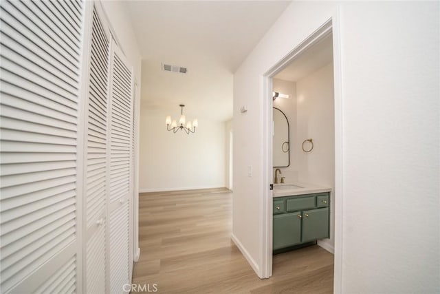 hallway featuring sink, light hardwood / wood-style flooring, and an inviting chandelier