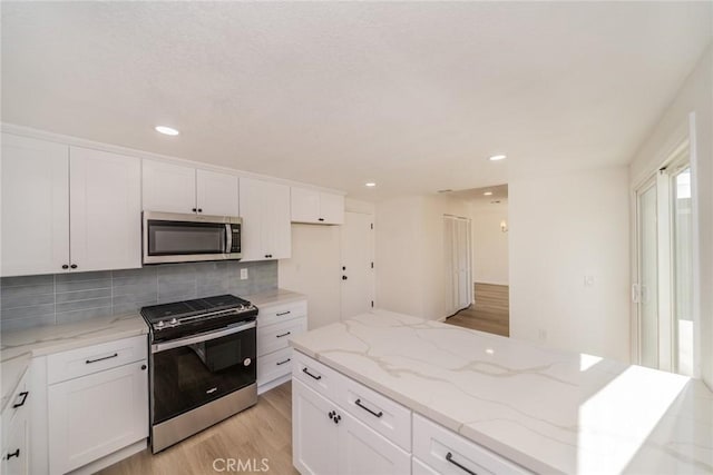 kitchen with light stone countertops, appliances with stainless steel finishes, white cabinetry, tasteful backsplash, and light hardwood / wood-style floors