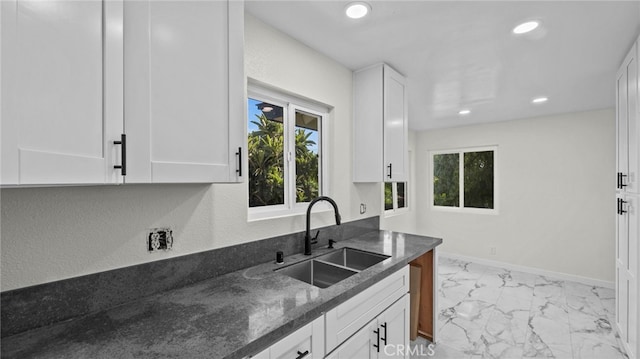 kitchen featuring dark stone countertops, white cabinets, and sink