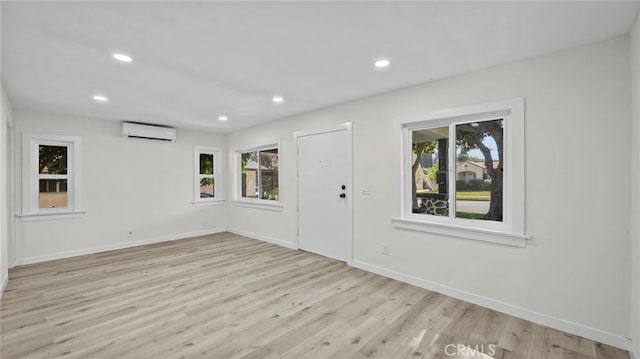 unfurnished room featuring a wealth of natural light, light wood-type flooring, and a wall mounted air conditioner