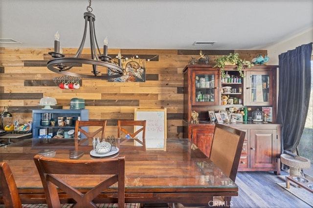 dining room with hardwood / wood-style flooring, wood walls, and a chandelier