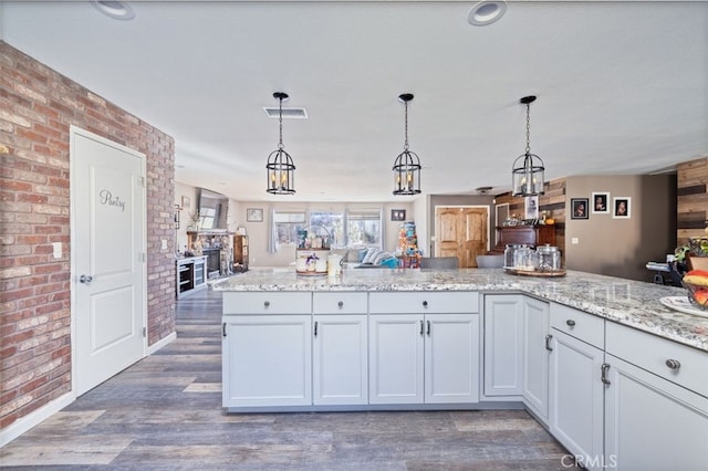 kitchen featuring decorative light fixtures, light stone countertops, dark wood-type flooring, white cabinets, and brick wall