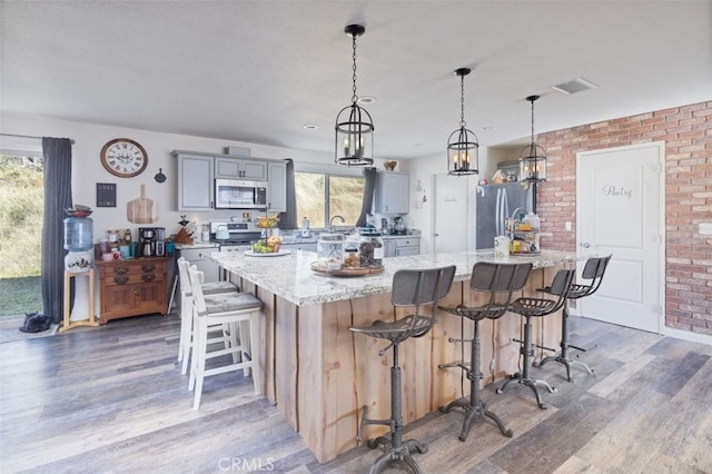 kitchen with a breakfast bar area, stainless steel appliances, gray cabinetry, a large island with sink, and light stone counters