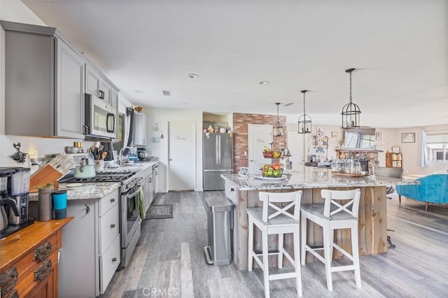 kitchen with a kitchen island, decorative light fixtures, stainless steel appliances, gray cabinets, and light stone counters