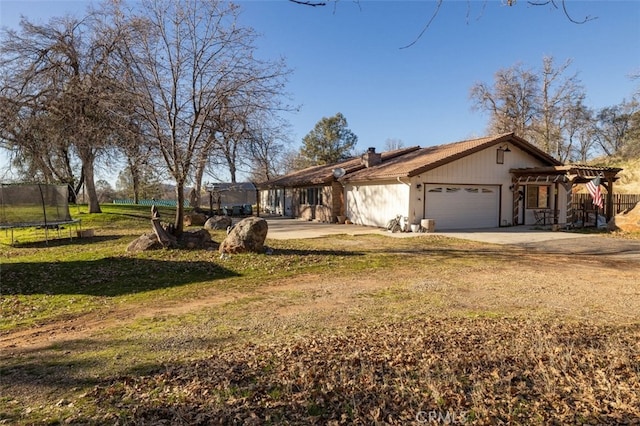 ranch-style home featuring a garage, a front yard, a pergola, and a trampoline