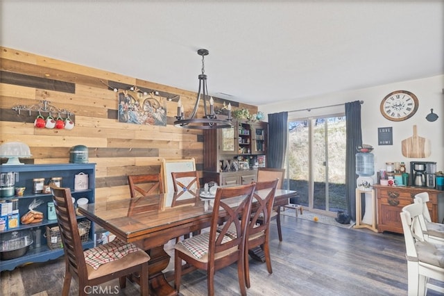 dining area featuring dark hardwood / wood-style floors, wood walls, and an inviting chandelier