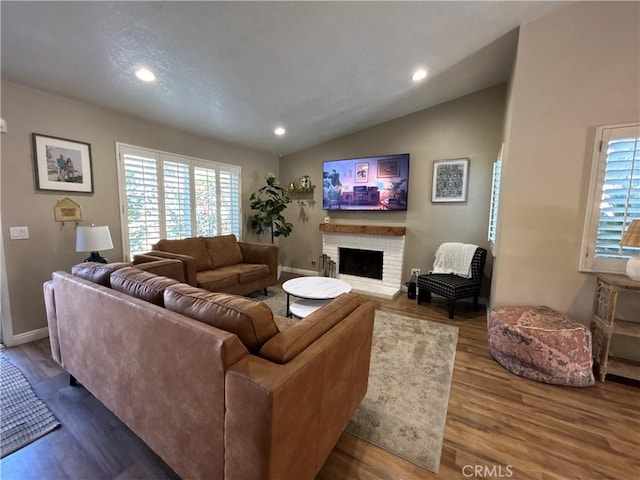 living room with hardwood / wood-style flooring, lofted ceiling, and a brick fireplace