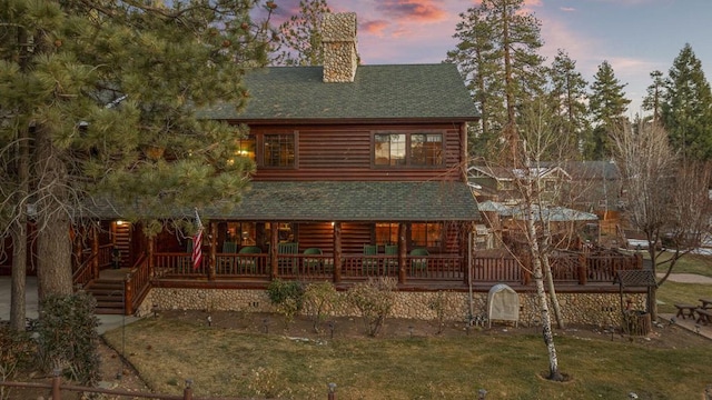 back house at dusk featuring a deck and a lawn