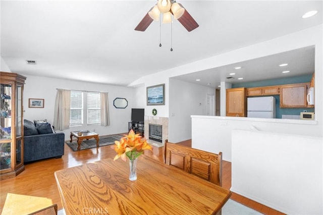 dining space with ceiling fan, a fireplace, and light hardwood / wood-style floors