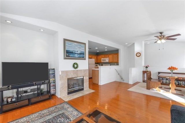 living room featuring ceiling fan, a tiled fireplace, vaulted ceiling, and light hardwood / wood-style floors