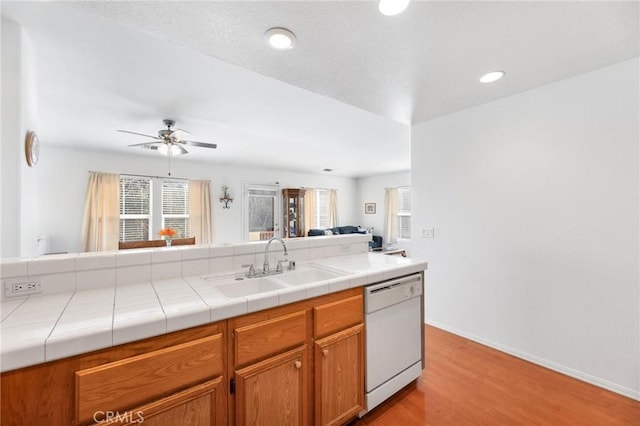 kitchen with tile countertops, ceiling fan, white dishwasher, light hardwood / wood-style flooring, and sink